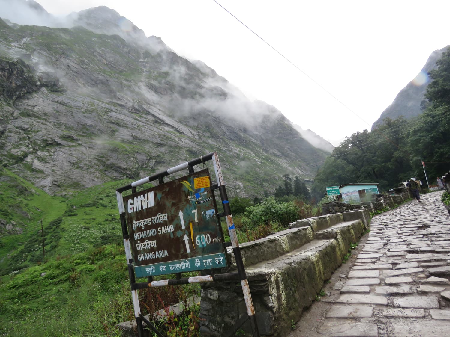 The stone-paved trail and a signboard near Ghangaria under cloud-covered valley walls