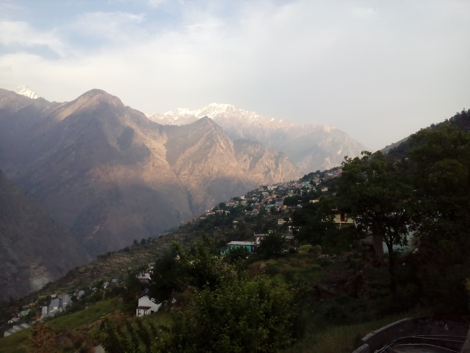 The town of Joshimath spread across a mountainside with snow peaks catching the light