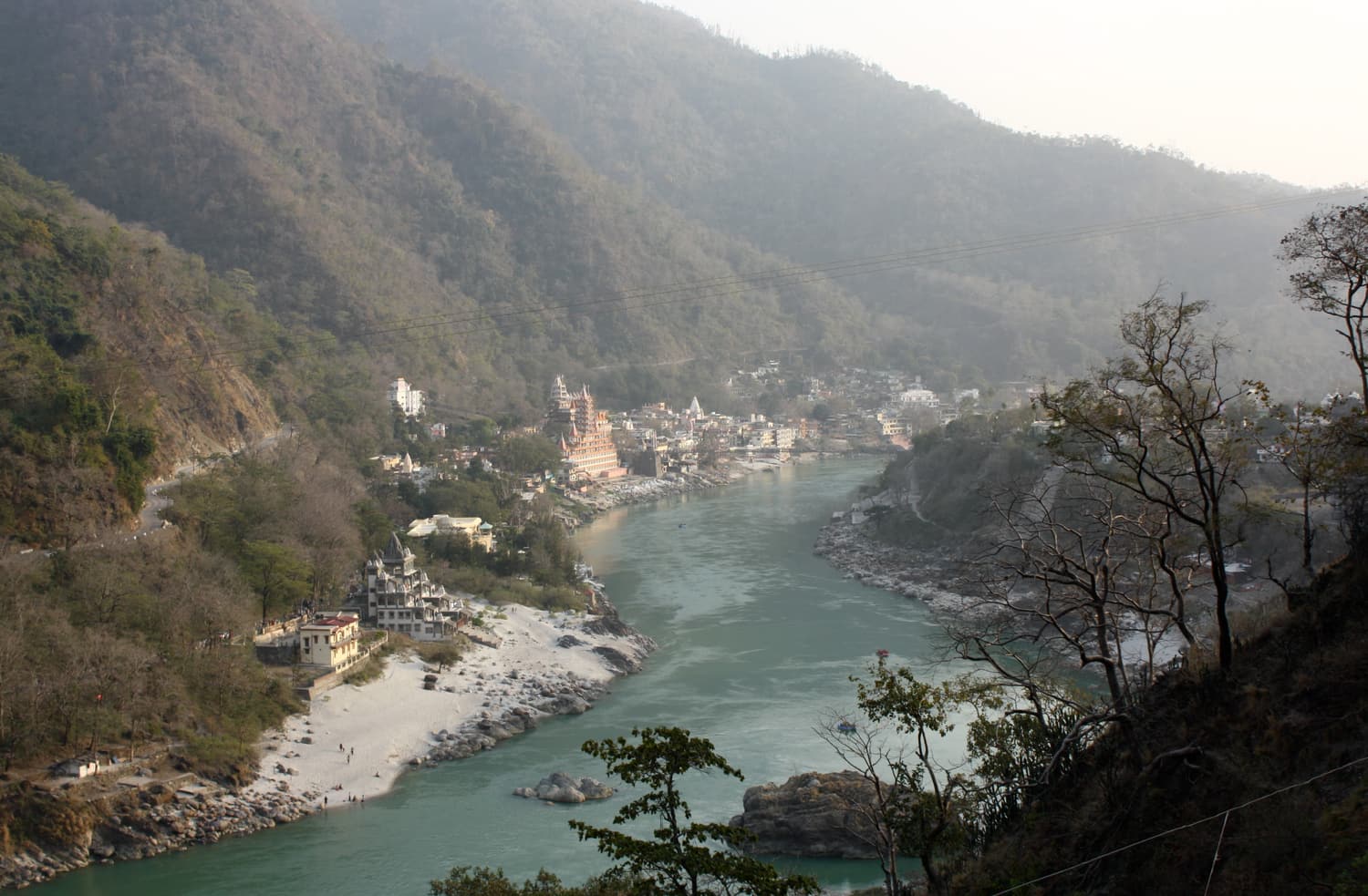 The Ganga flowing between forested hills at Rishikesh with temples on the far bank