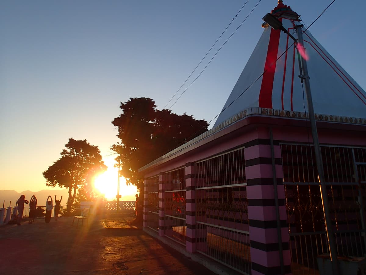 The sun rising beside the red-and-white Kunjapuri temple above Rishikesh